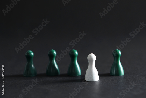 Choice concept. White pawn and green ones on dark table