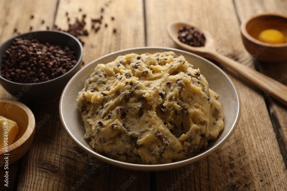 Chocolate chip cookie dough in bowl and ingredients on white wooden table, closeup Chocolate chip cookie dough in bowl and ingredients on white wooden table, closeup