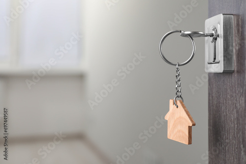 Mortgage and real estate. Open door with key and house shaped keychain against blurred background, space for text