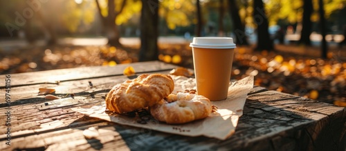 Eco-friendly cup with a drink and pastry, on paper and wood. Street or park breakfast.