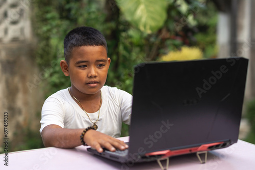 Obraz na plátně A young tech savvy rural asian boy typing on a laptop