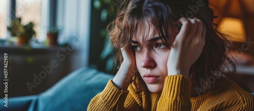 Woman experiencing headache and stress at home, dealing with anxiety, depression, and debt. Upset girl in living room facing a crisis, psychological issues, and the repercussions of mistakes, feeling photo