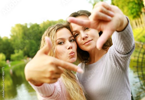 Lifestyle, family and people concept: mature mother and adult daughter are doing selfie by mobile phone in summer park.