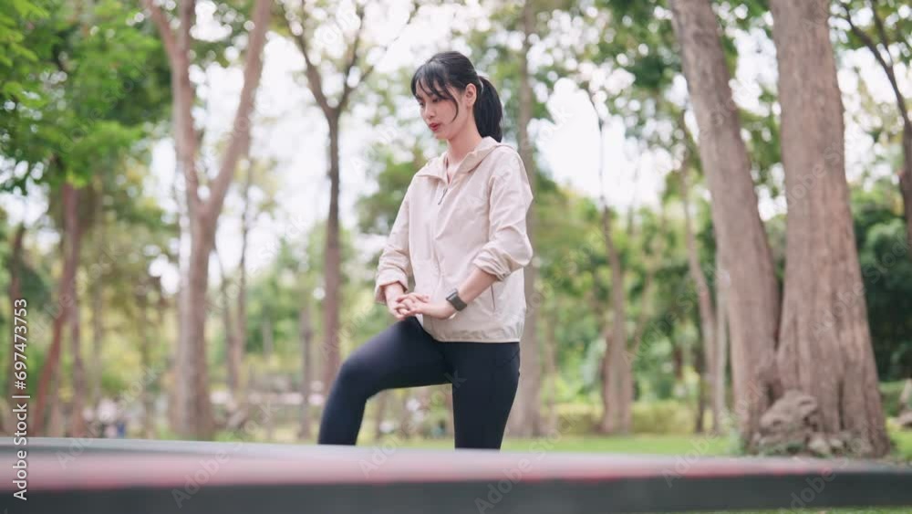 An Asian woman in workout attire is doing leg stretches, preparing her body for exercise in a public park. Showcase the flexibility and warm-up routine for a fitness session outdoors An Asian woman in workout attire is doing leg stretches, preparing her body for exercise in a public park. Showcase the flexibility and warm-up routine for a fitness session outdoors
