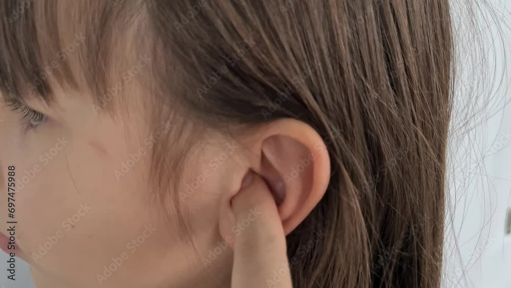 Closeup of part of child head, girl scratches ear with hand. Touching a finger inside and modern hygiene concept Closeup of part of child head, girl scratches ear with hand. Touching a finger inside and modern hygiene concept