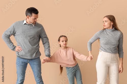 Sad little girl with her divorced parents on beige background