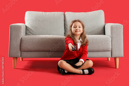 Cute little girl watching TV near grey sofa on red background
