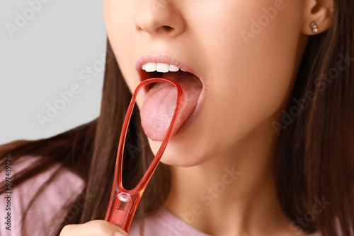 Young woman with tongue scraper on grey background