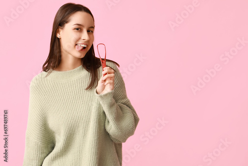Beautiful young woman with tongue scraper on pink background