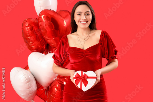 Young couple with gift and heart-shaped balloons on red background. Valentine's Day celebration © Pixel-Shot