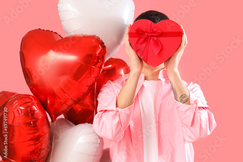Young man with gift box and heart-shaped balloons on pink background. Valentine's Day celebration © Pixel-Shot