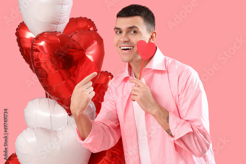 Young man with paper heart and balloons on pink background. Valentine's Day celebration © Pixel-Shot