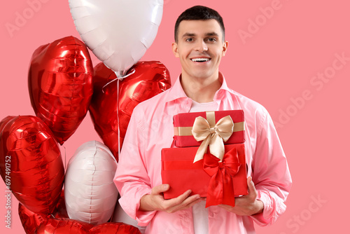 Young man with gifts and heart-shaped balloons on pink background. Valentine's Day celebration © Pixel-Shot