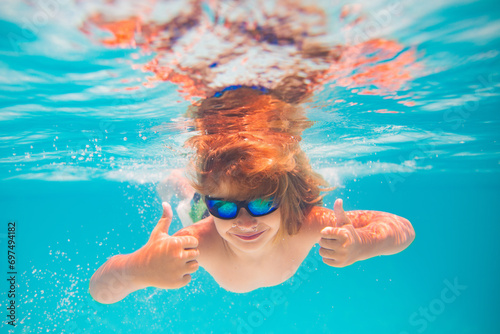 Kid swimming in pool underwater. Child boy swim underwater in sea. Child playing and diving in swimming pool. Funny kids boy play and swim in sea or pool water. Summer vacation concept.