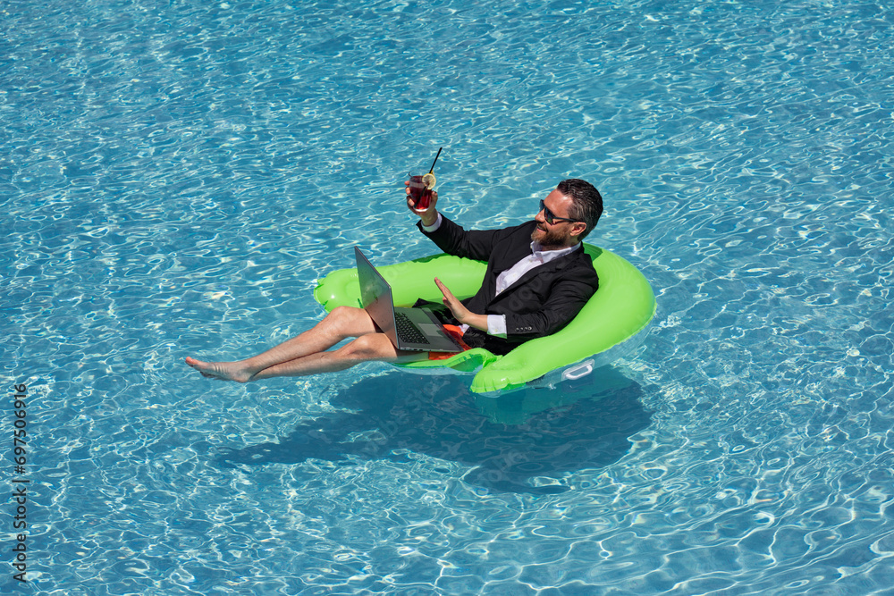 Summer business dreams. Business man in suit floating with cocktail and laptop in swimming pool. Summer business vacation. Funny crazy businessman rest in formal wear in pool. Hot summer business.