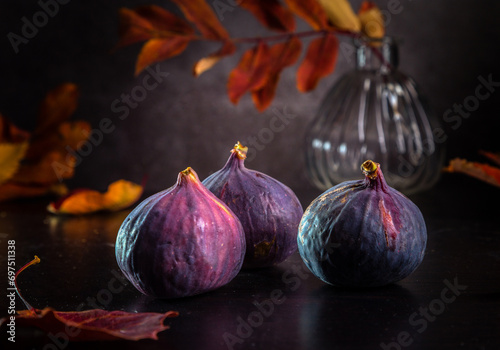 Fresh figs and autumn leaves lie on a dark wooden table. Beautiful large blue fig fruits.