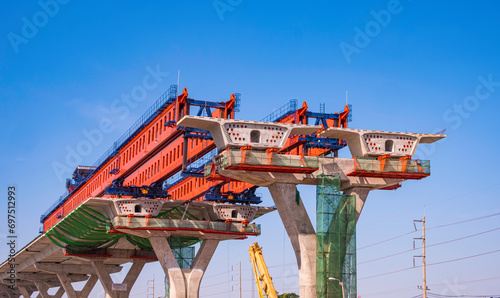 Metal launching gantry structure for installing concrete typical segment joint on foundation of elevated expressway in road construction site against blue sky background