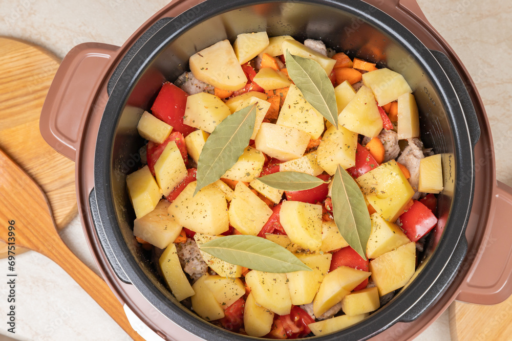 Modern, light multi cooker with products. Cooking stewed potatoes with meat in multicooker. Close-up top view of multi cooker with vegetables and meat.