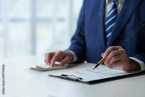Businessman uses pen to point at chart Graph and use ideas to analyze financial reporting situations. Calculate your investments with the income, tax and accounting calculators at your desk. photo
