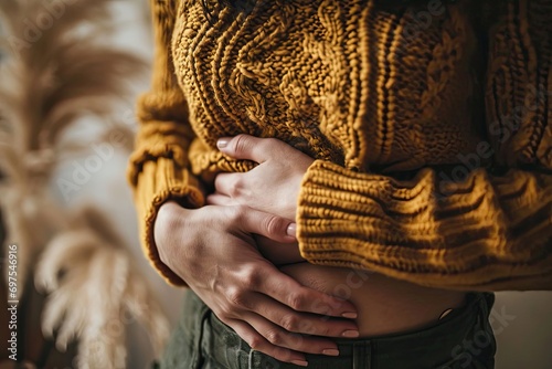 A woman in a sweater is holding her stomach. A person experiences abdominal pain. The girl's face is not visible. Free space