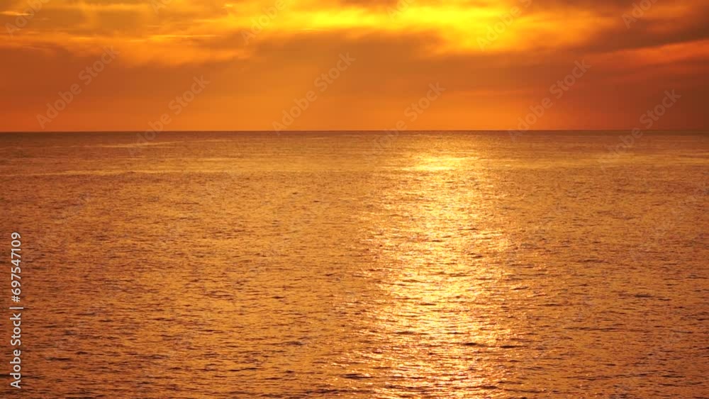 A red burning sunset over sea with rocky volcanic cliff. Abstract nature summer ocean sea background. Small waves on golden warm water surface with bokeh lights from sun. Weather and climate change A red burning sunset over sea with rocky volcanic cliff. Abstract nature summer ocean sea background. Small waves on golden warm water surface with bokeh lights from sun. Weather and climate change