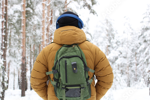 young man wearing headphones walks in a snowy forest. guy enjoys the winter nature in the park.