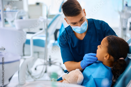Dentist examining teeth of little black girl at dental clinic.