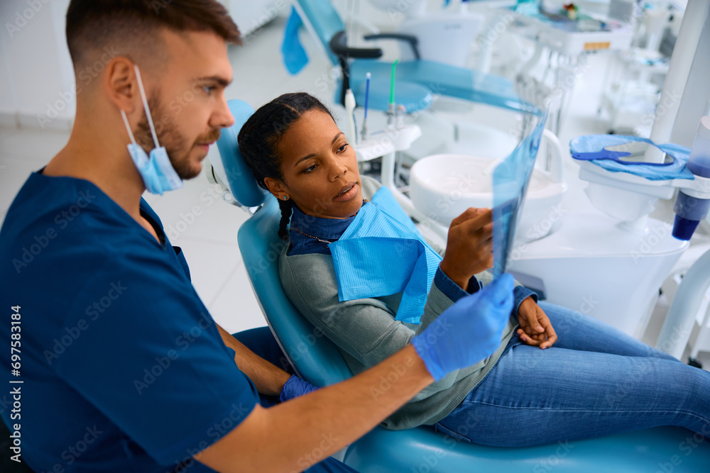 Obraz premium Black woman and her dentist examining dental X-ray during appointment at dental clinic.