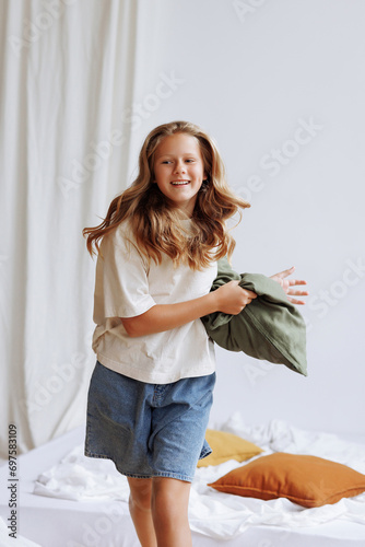 Caucasian girl  around 7  in white tee and blue shorts holds a green pillow. Minimalist interior  white backdrop. Concept for home comfort or kids apparel ads.