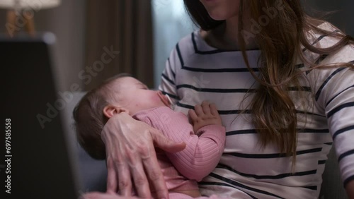 Mother working online while maternity leave. Woman holding daughter with pacifier in mouth. Woman using laptop for working online. Close up of baby girl sleeping on mother hands. photo