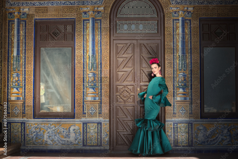 Young, pretty, blonde woman in typical green colored flamenco suit, posing with beautiful tiled wall in background. Flamenco concept, typical Spanish, Seville, Andalusia.