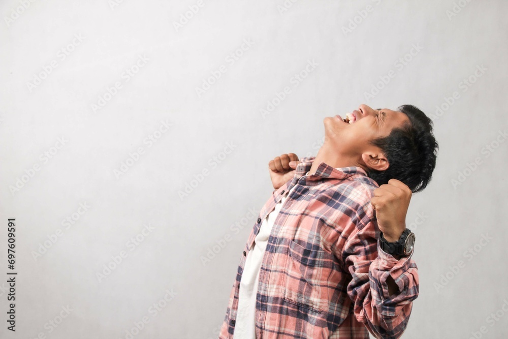 Young Asian man in long pink shirt looking to the side with successful hand gesture, happy face up. isolated white background