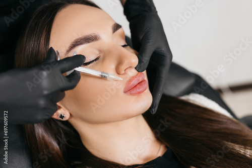 Close-up of a woman's face. A cosmetologist in medical gloves pierces a woman's lip with a syringe with hyaluronic acid. lip augmentation procedure. beauty injections. Cosmetological injections