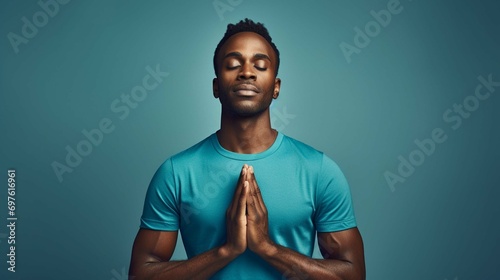 Calm dark skinned man enjoys morning yoga practicing breathing exercises for inner peace and harmony meditates and keeps hands in okay gesture wears black t shirt isolated over blue background