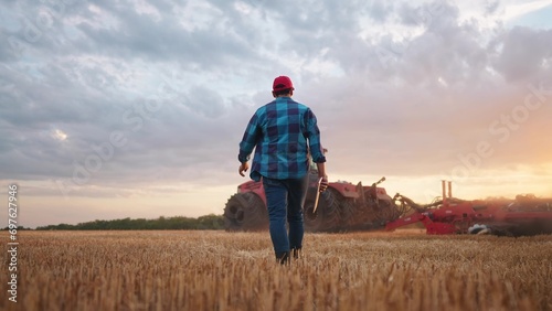 agriculture. farmer walk works in a field next to a tractor that plows the land. business agriculture concept. farmer with tablet works in a field next to a tractor at farm sunset mowed wheat plows