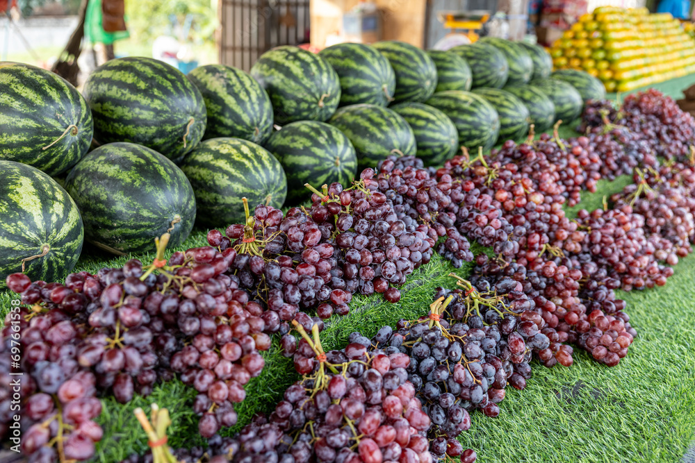 Close-up view of piles of purple grapes and watermelons stacked.