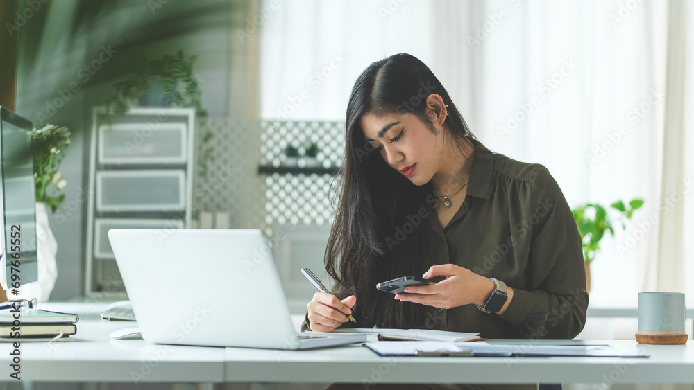 Beautiful asian businesswoman sitting at her workplace and using smart phone. Beautiful asian businesswoman sitting at her workplace and using smart phone.