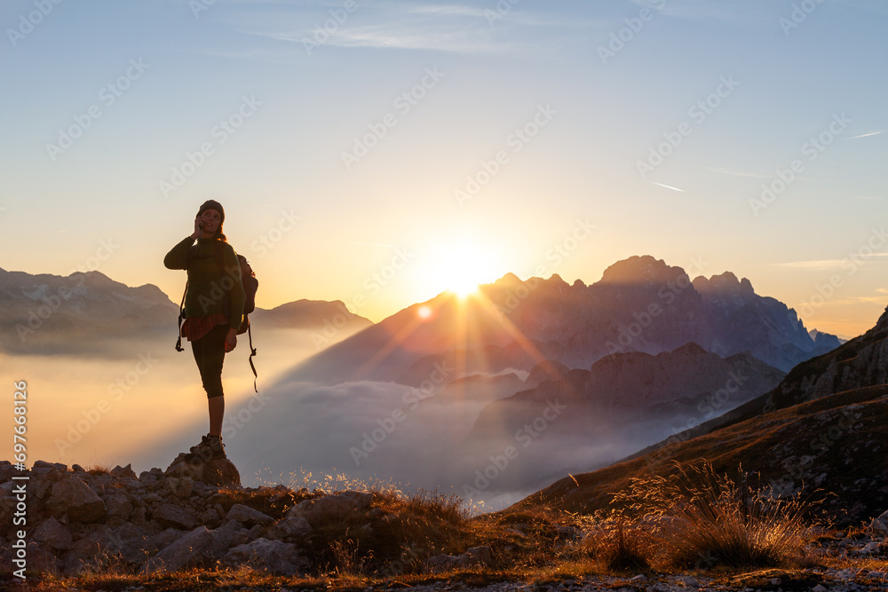 Woman Solo Hiker Talking on her Mobile Device Smart Phone From a Remote Location Above Clouds at Sunset in High Mountains
