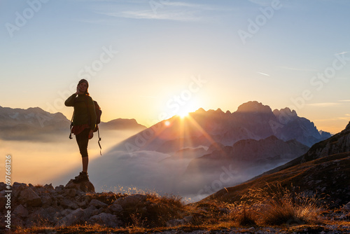 Woman Solo Hiker Talking on her Mobile Device Smart Phone From a Remote Location Above Clouds at Sunset in High Mountains
