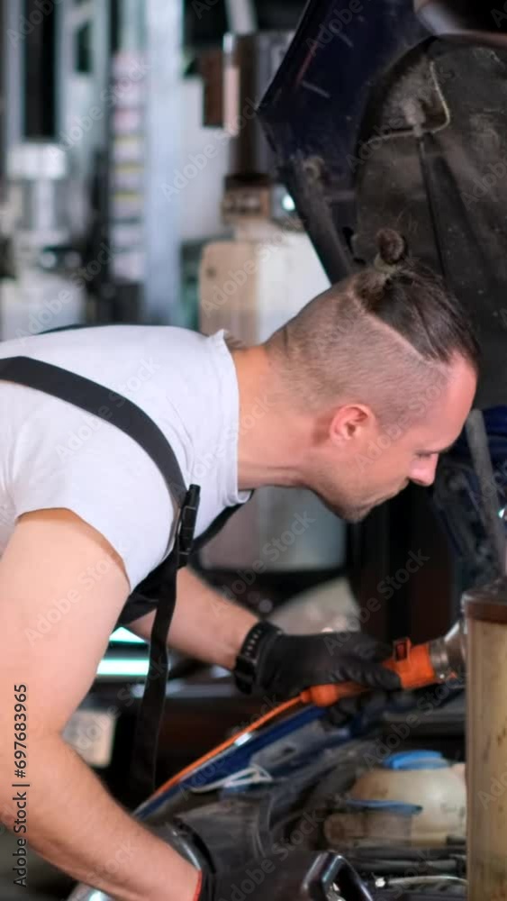 A professional auto mechanic changes the engine oil in a car engine at a service station. Vertical video A professional auto mechanic changes the engine oil in a car engine at a service station. Vertical video