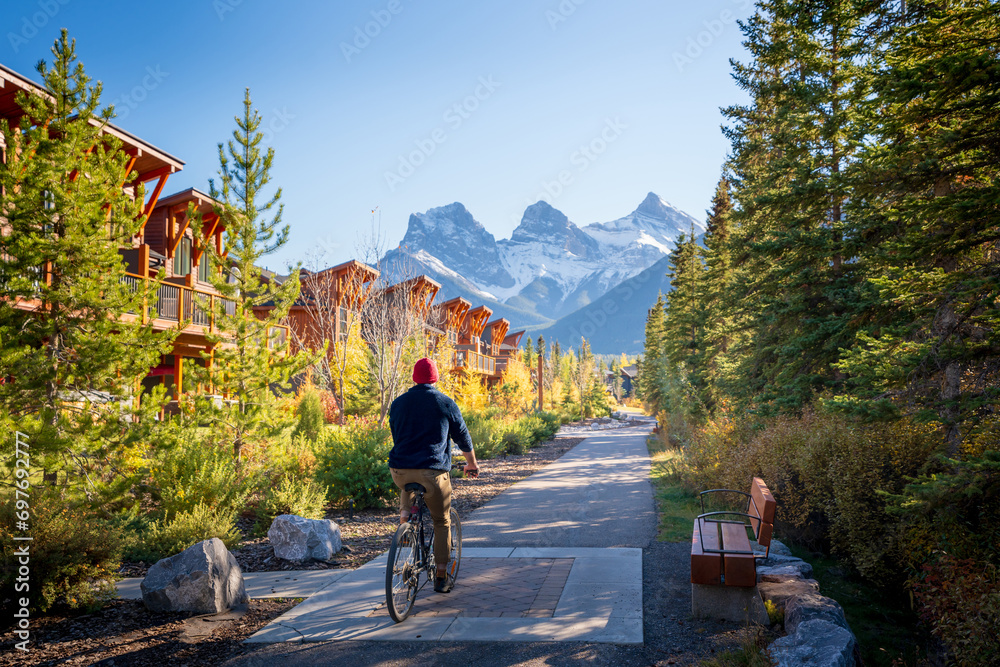 People riding a bicycle on trail in residential area. Town of Canmore street view in fall season. Alberta, Canada. - obrazy, fototapety, plakaty 