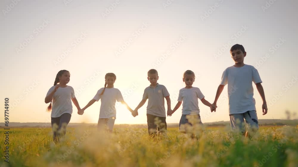 a group of children walk across the field on the grass. lifestyle happy family childhood dream concept. kids walking in a field with tall grass on the sunset and holding lifestyle their hands a group of children walk across the field on the grass. lifestyle happy family childhood dream concept. kids walking in a field with tall grass on the sunset and holding lifestyle their hands