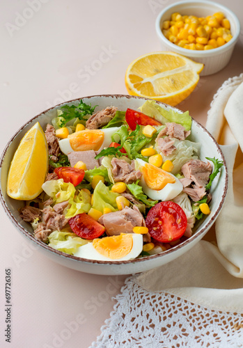 Fresh salad of tuna, egg, lettuce, cherry tomatoes, corn and lemon on a light background. Healthy nutrition concept, full bowl of salad.