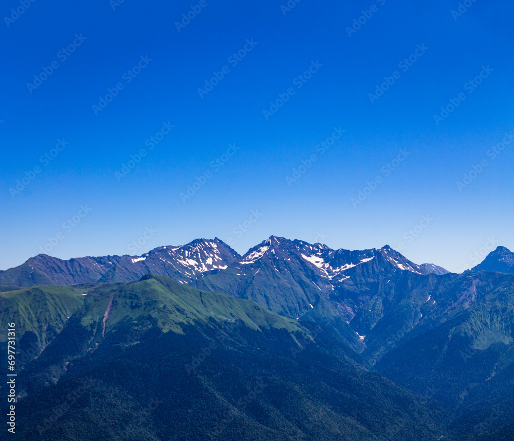 Beautiful mountain landscape with a green picturesque mountain range against a blue sky. Snow lying in the mountains even in summer.