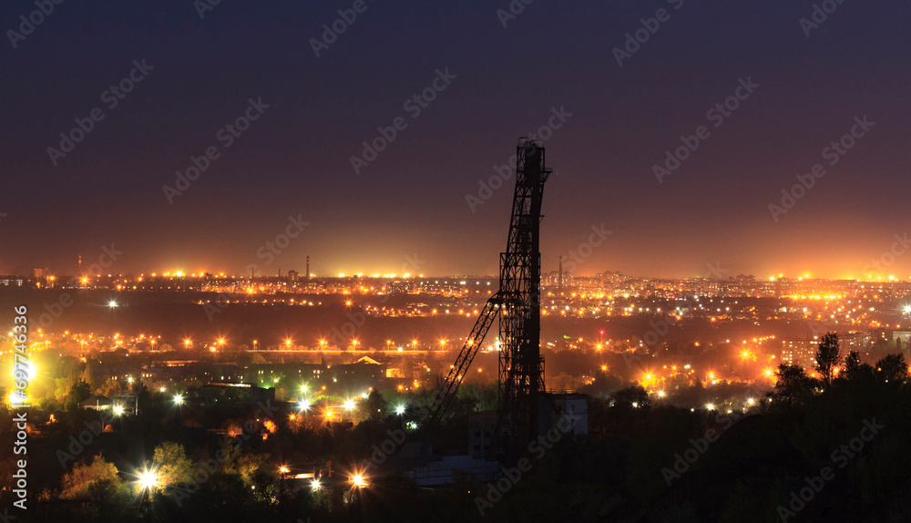 Mine pile driver over the silhouette of a night industrial city