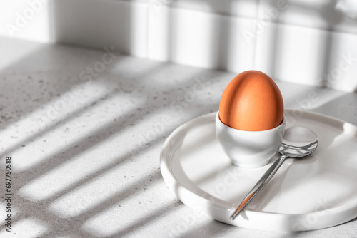 Boiled egg in hard light with window shadows on white kitchen background. Light protein breakfast concept, minimalism, high key photo
