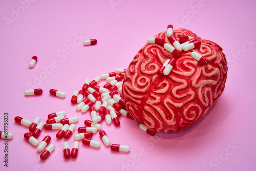 Red human brain with a pile of red and white pills and capsules on a pink table.