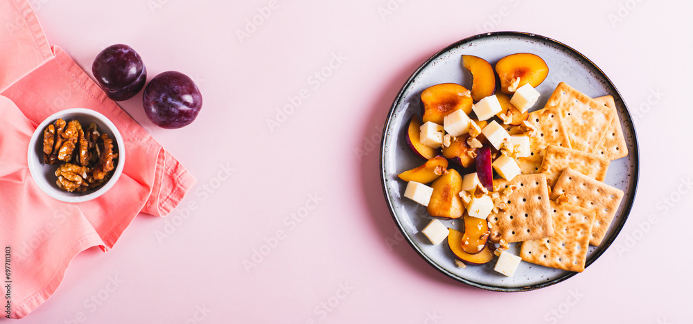 Dinner for girls, biscuits, cheese, plums and walnuts on a plate on pink top view web banner Dinner for girls, biscuits, cheese, plums and walnuts on a plate on pink top view web banner