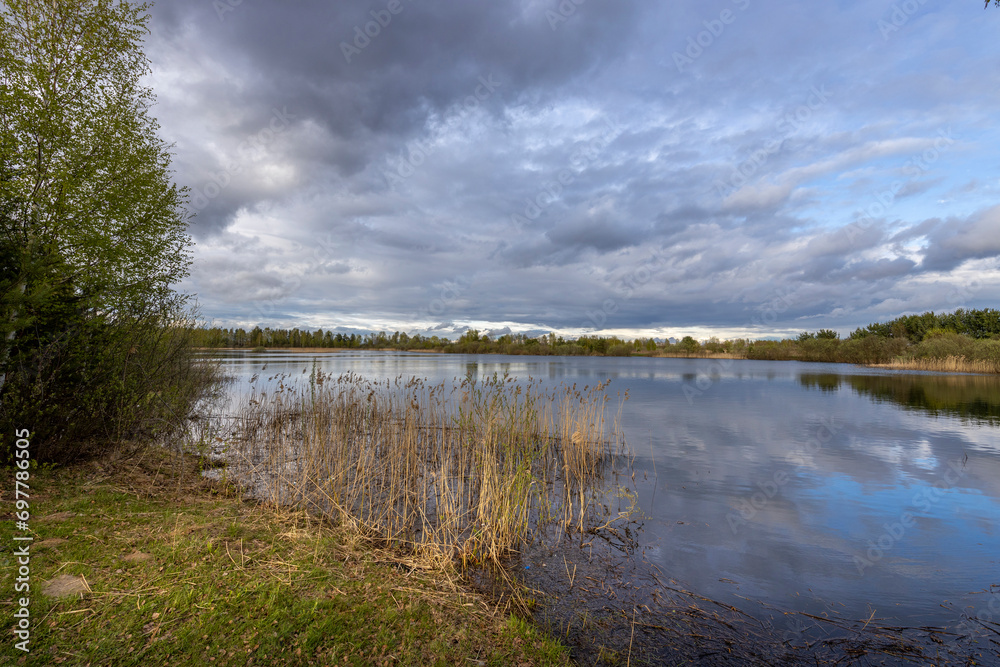 Spring landscape with a pond and sky. young green grass in the foreground. strip of forest on the horizon. clouds reflected in the water