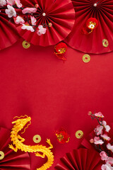 Decorating for Chinese New Year concept. Top view vertical photo of gold dragon, paper fans, lucky coins, decorative elements, sakura on red background with advert space